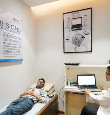 Man laying down on a bed next to an audiologist with a laptop in a clinic